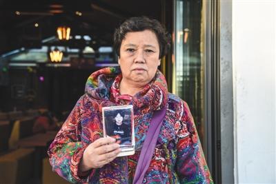11月9日，北京什刹海公园，李艳霞手持儿子的照片在一家酒吧门前。