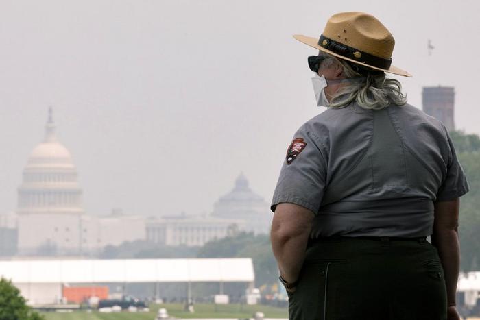 6月29日，在美国首都华盛顿，国家公园的一名员工戴着口罩工作，远处的国会大厦笼罩在烟雾中。