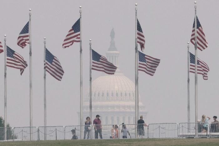 6月29日，在美国首都华盛顿，游客在华盛顿纪念碑游览，远处的国会大厦笼罩在烟雾中。
