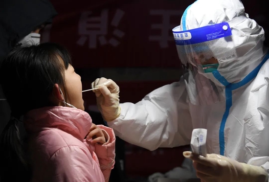  12月25日晚，在西安市莲湖区劳动路核酸采样点，医务人员为小朋友进行咽拭子采样。图源：新华社