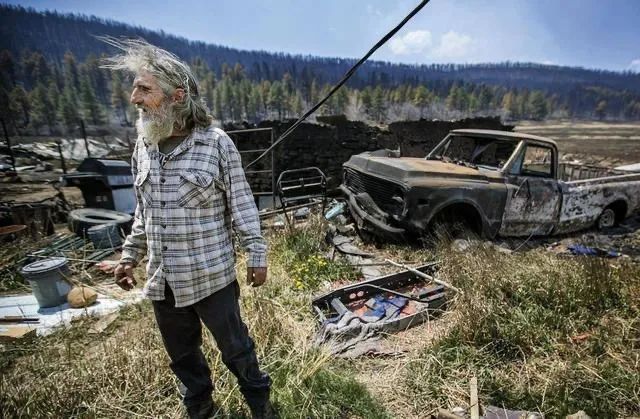 2022年5月4日，在美国新墨西哥州莫拉附近，一名居民站在被山火烧毁的房屋和车辆前