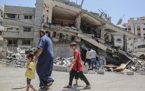 资料图：巴勒斯坦人走在被以色列空袭摧毁的房屋废墟旁。