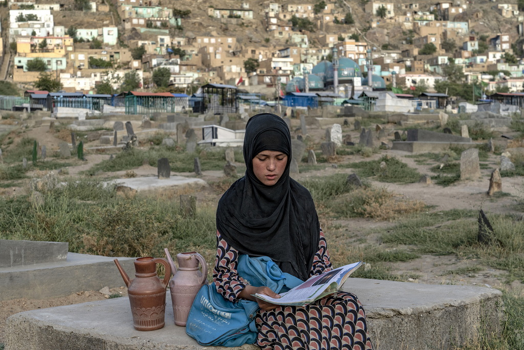 当地时间2022年7月30日，阿富汗首都喀布尔，14岁的阿富汗女孩Sara坐在墓地边看书边等待顾客买水。 视觉中国 图