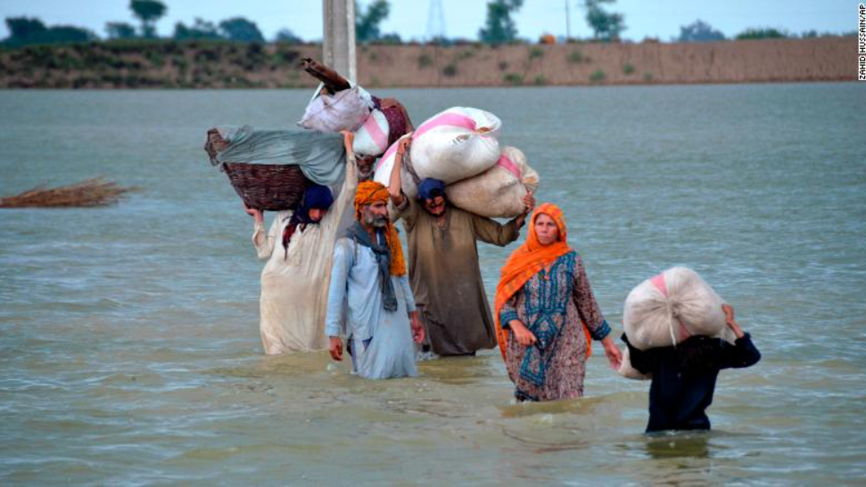 24 日，俾路支省一个流离失所的家庭涉水穿过洪水区。图源：CNN