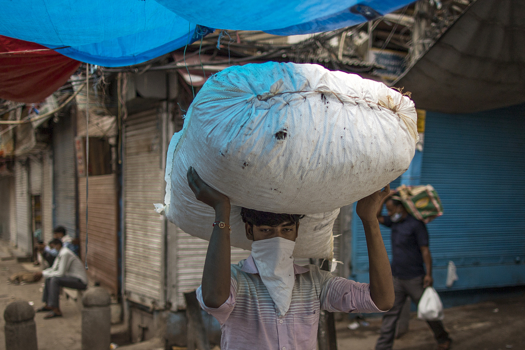 当地时间2020年8月31日，印度新德里，戴着口罩的搬运工头上顶着一个袋子。人民视觉 资料图