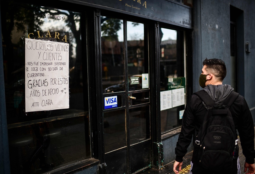 阿根廷布宜诺斯艾利斯，一名男子走过一家关门的餐馆，招牌上写着:“亲爱的邻居和客户们，隔离80天，我们难以维持。” 图源 视觉中国