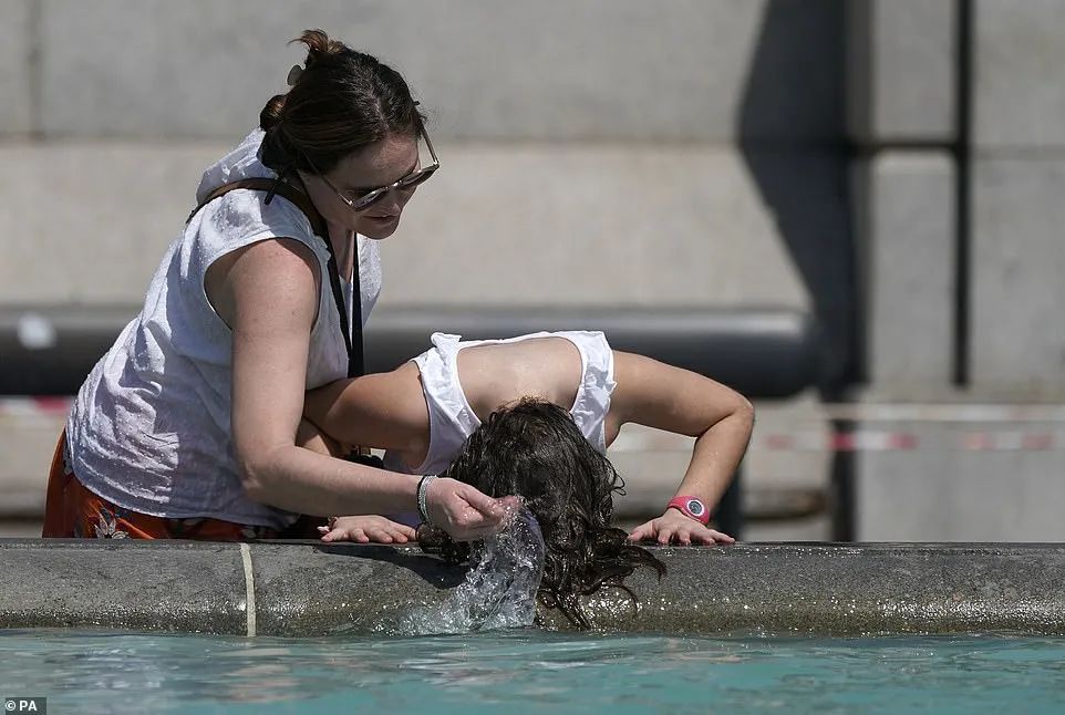 7月19日，在伦敦特拉法加广场，一名女子把头伸进喷泉里降温